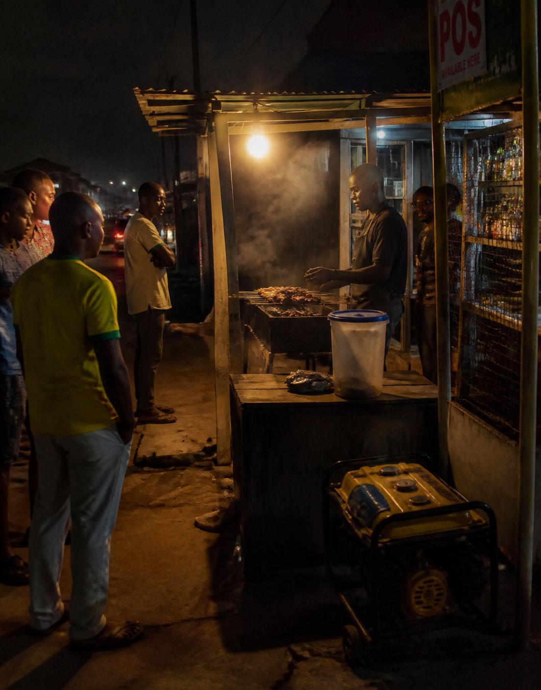 A roadside suya grill lit by a single bulb at night